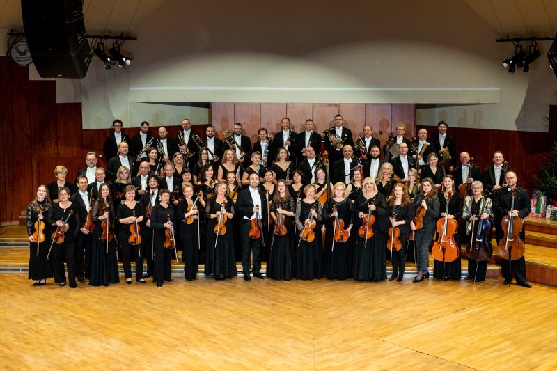 Zdjęcie przedstawia orkiestrę w strojach galowych wraz z instrumentami