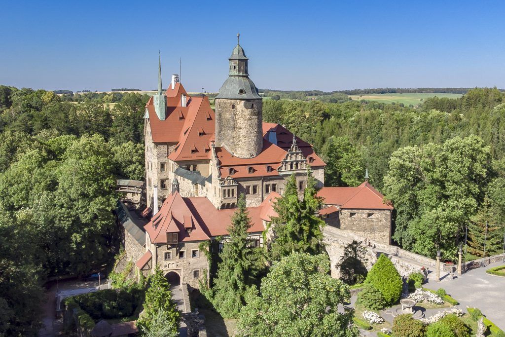 Widok z góry na dawny zamek z czerwonymi dachówkami, wieżą otoczony drzewami