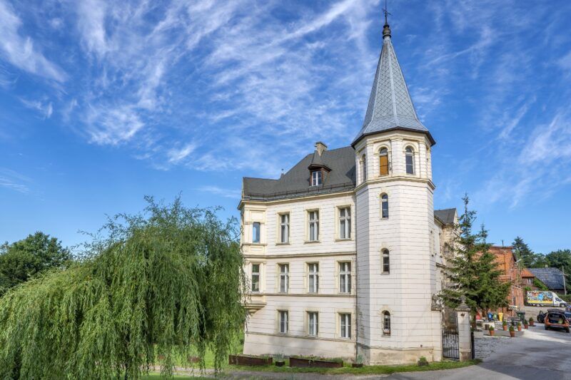 Widok na pałac, z jasną elewacją, w tle błękitne niebo.
