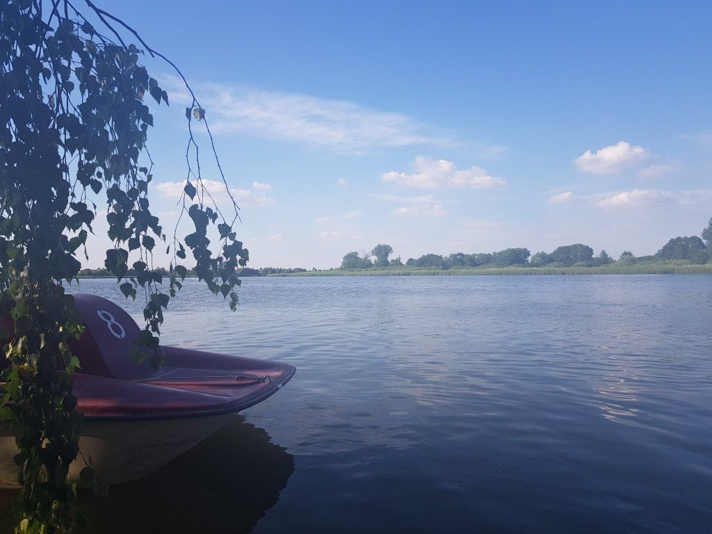Jezioro z łódką przy brzegu, w oddali brzeg z drzewami