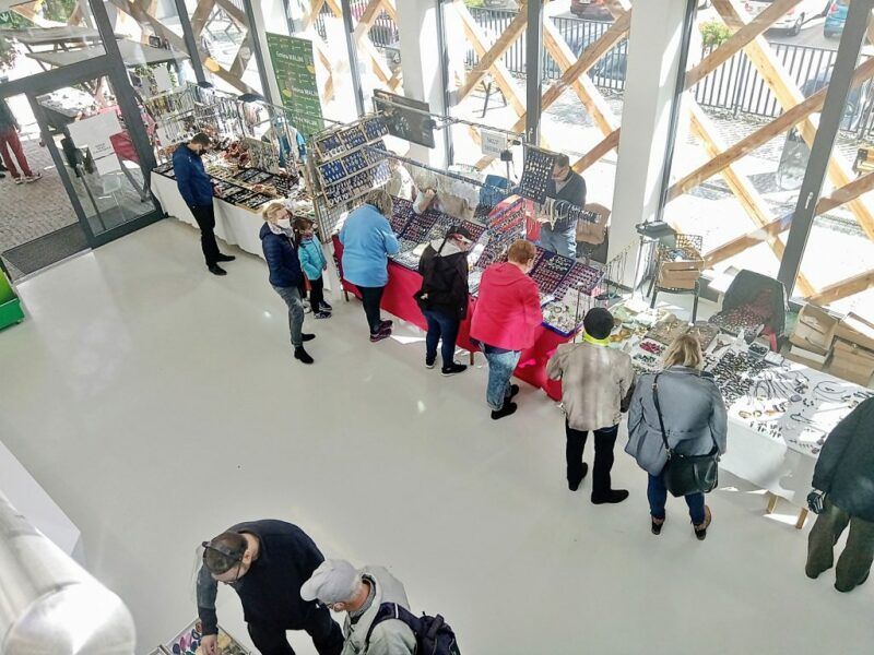Wnętrze Centrum Obsługi Ruchu Turystycznego "Akwarium"w którym znajdują się ludzie stojący przy różnych stanowiskach informacyjnych. Na zdjęciu widać przeszklone szyby a w środku jest jasno