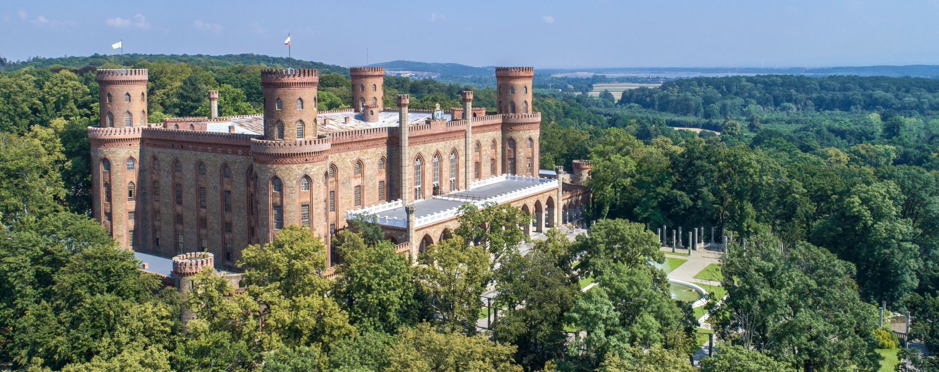 Panorama na Pałac z czterema wieżami leżący na wzgórzu otoczony drzewami