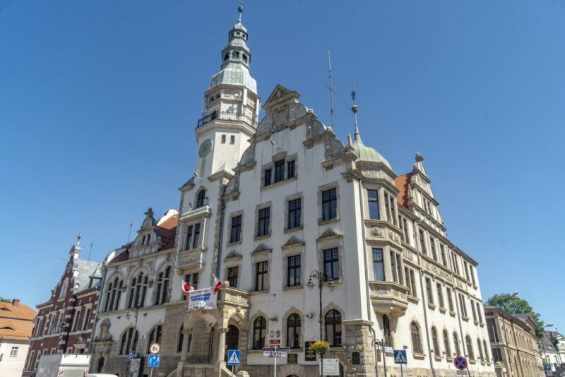 Ratusz z białą elewacją, z szarą dekoracją wokół okien, w tle błękitne niebo.