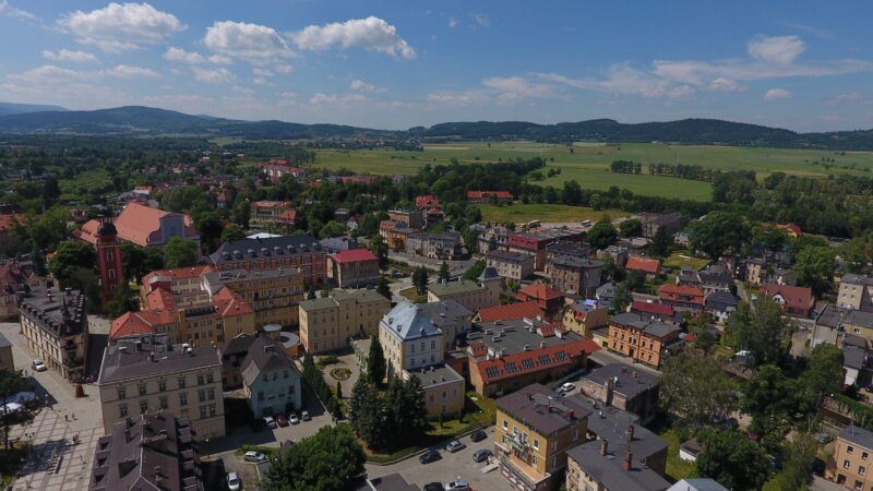 Widok na miasto z lotu ptaka, w tle góry, błękitne niebo.