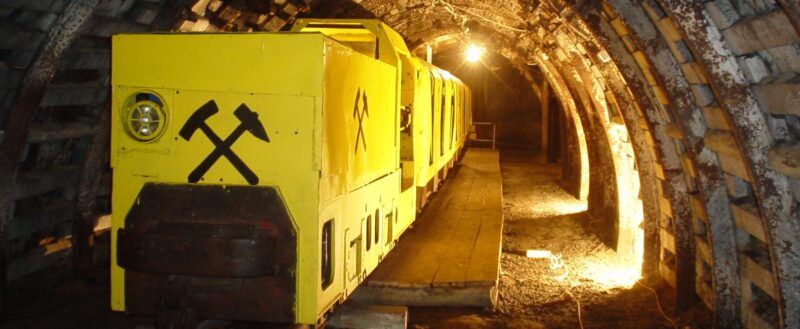 Żółte wagoniki kolei w oświetlonym tunelu kopalni.