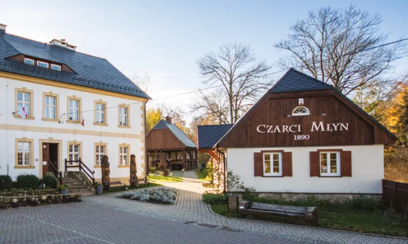 Widok na niewielką, odnowioną chatę sudecką z napisem Czarci Młyn