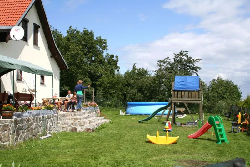 Trawiaste podwórze kempingu w Mirsku oferuje basen i kolorowy plac zabaw dla dzieci, obok białego domu z kamiennym tarasem i ogrodem.