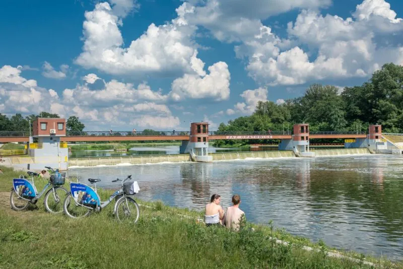 Widok na jaz w Opatowicach z grupą rowerzystów odpoczywających u brzegu