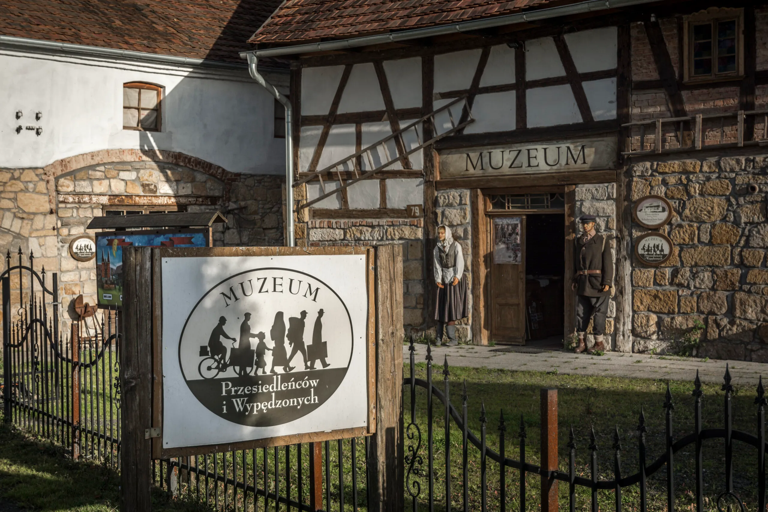 The stone-half-timbered facade of the Museum of Displaced Persons and Expellees in Pławna is decorated with signs, paintings, and a wrought-iron entrance gate.