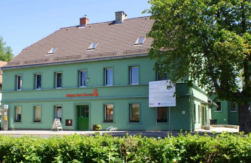 Zielony budynek z czerwonym dachem, w którym znajduje się dom kultury