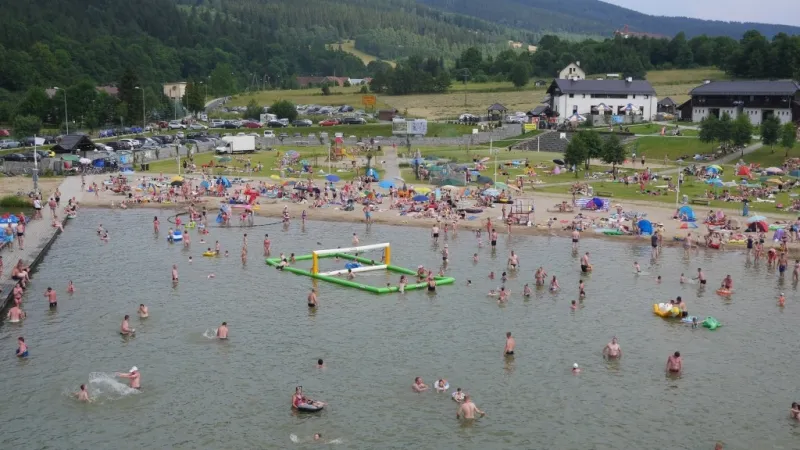 Tłumy plażowiczów kąpią się w płytkim zalewie i odpoczywają na piaszczystym brzegu, korzystając z dmuchanego toru przeszkód, leżaków i zabawek wodnych.