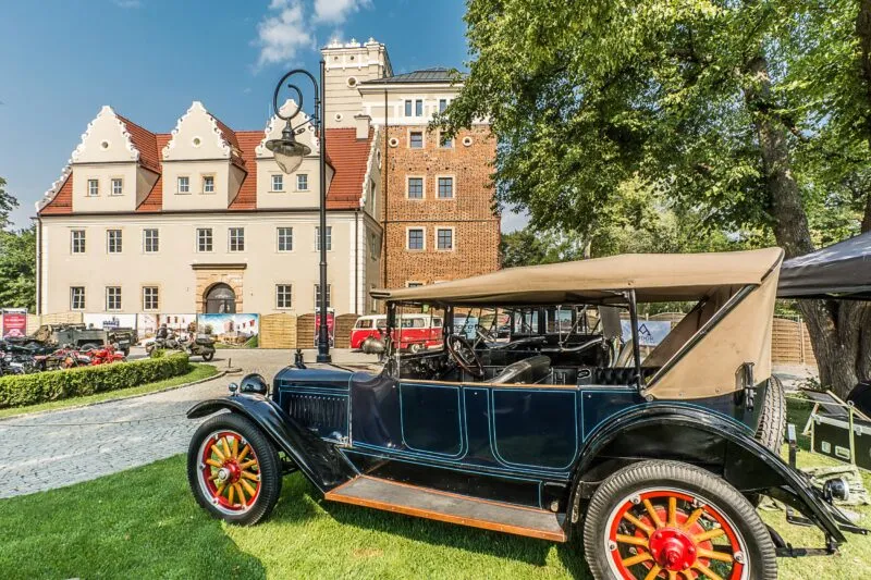 Zabytkowy czarny samochód na trawie, w tle drzewa i budynek.