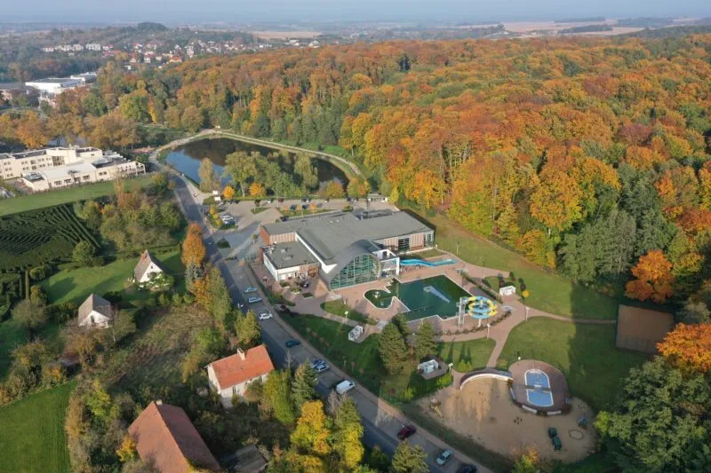 Zdjęcie przedstawia widoczny z góry ośrodek sportowy w otoczeniu lasu. Na jego terenie znajdują się zjeżdżalnie oraz baseny.
