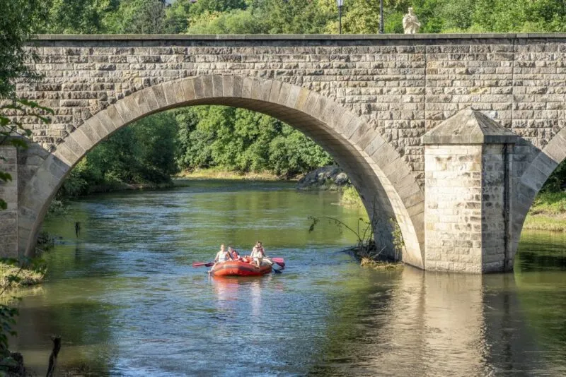 Most kamienny nad rzeką, pod nim przepływa czerwony ponton.