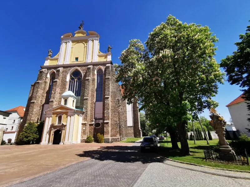 Zdjęcie przedstawia kościół z szarych cegieł, niektóre części pokryte są żółto-białą elewacją.