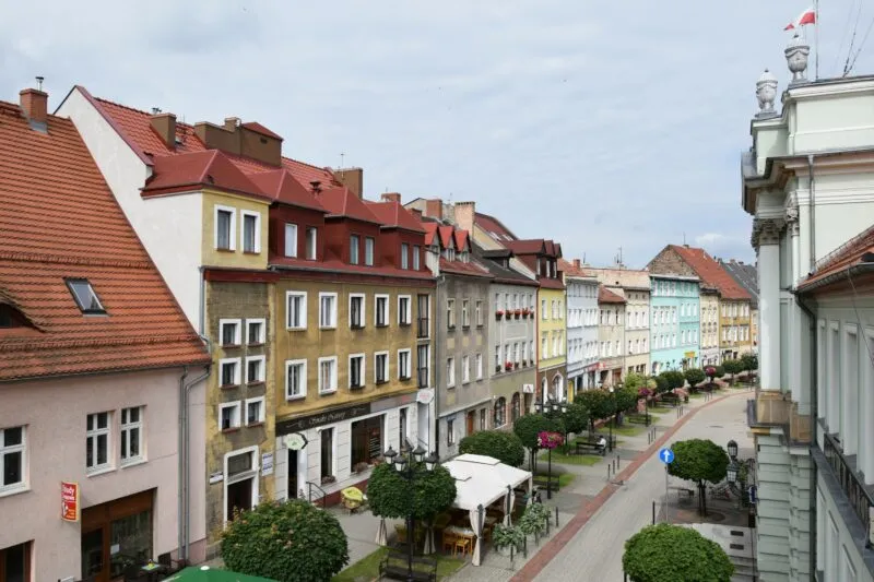 Dwa rzędy różnokolorowych kamienic. Na środku, pomiędzy nimi ogródki restauracyjne, elementy zieleni miejskiej.