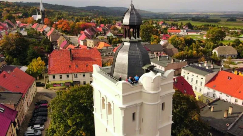 Widok z poziomu szczytu białej wieży widokowej w Złotym Stoku z okolic złotostockiego rynku. Widoczna panorama Sudetów i okolic Złotego Stoku.