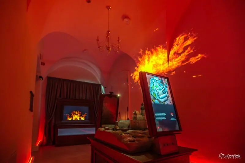 A red projection of flames fills the wall of the darkened room at the Nature and Education Center in Sobieszów, next to an interactive screen and a display case.