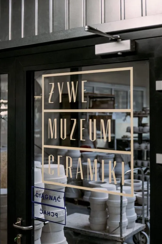 Zbliżenie na logo Żywego Muzeum Ceramiki ujęte na szklanych drzwiach wejściowych