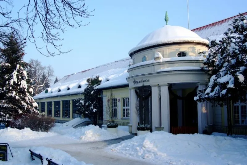 Zimowy widok na wejście do zabytkowego ośnieżonego budynku uzdrowiska.