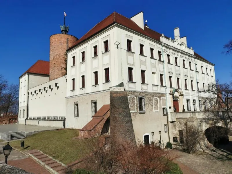 Jasny budynek z dużymi oknami i czerwonym dachem oraz wieżą z czerwonej cegły przy bezchmurnym niebie