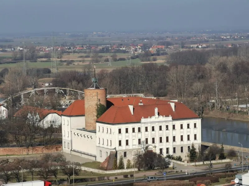 Biały budynek Zamku Książąt Głogowskich z czerwonym dachem widoczny z oddali w pełnej okazałości