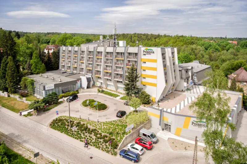 Zdjęcie wykonane z drona, przedstawia masywny, wielopiętrowy budynek hotelowy z podjazdem i parkingiem