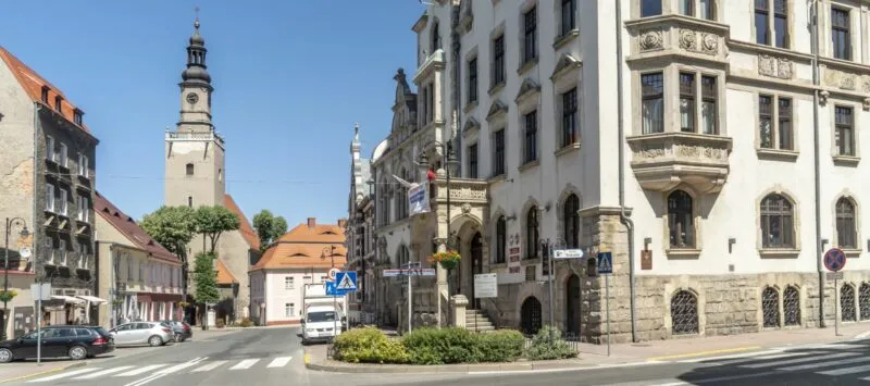 Zdjęcie przestawia ulicę w Kamiennej Górze, po prawej stronie budynek z jasną elewacją, w tle kościół.