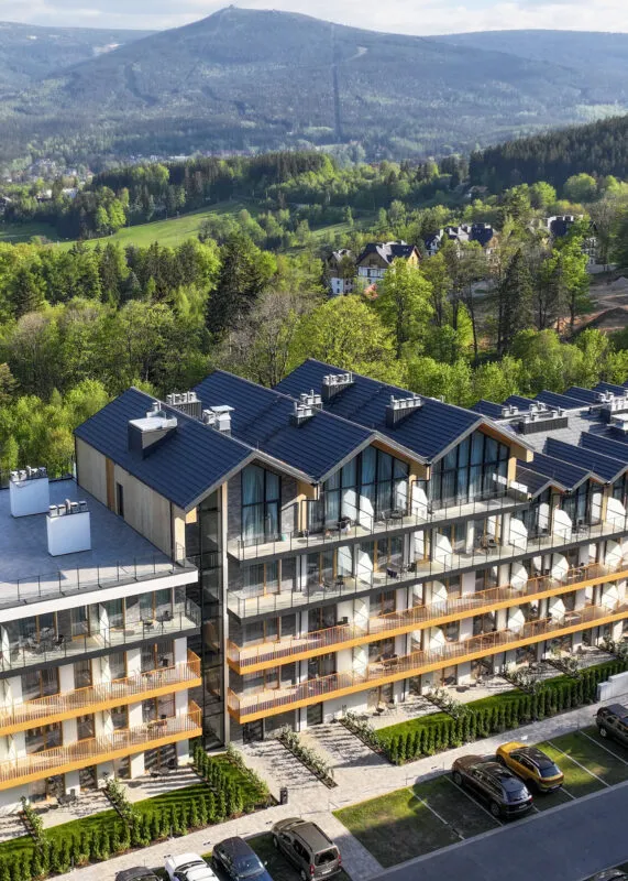 Widok z lotu ptaka na resort - elegancki budynek o przytulnym górskim charakterze, z dużymi oknami i balkonami, w tle góry.