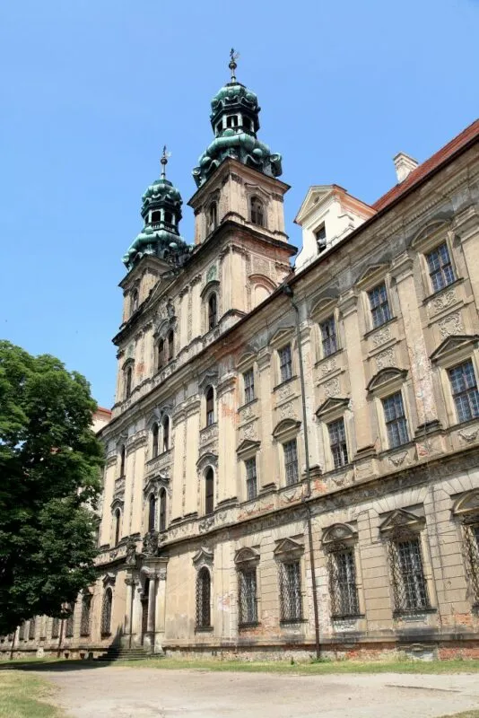 Barokowe mury opactwa zwieńczone dwiema wieżyczkami z dachem pokrytym seledynowym kolorem.