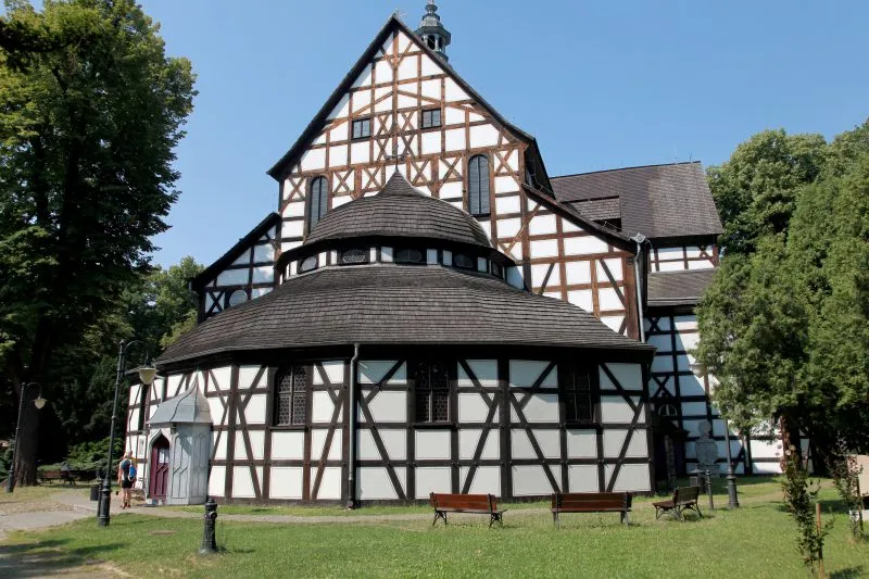 Kościół Pokoju w Świdnicy prezentuje charakterystyczną biało-brązową konstrukcję szachulcową, wieloboczną kruchtę i stromy dach pośród wysokich drzew.