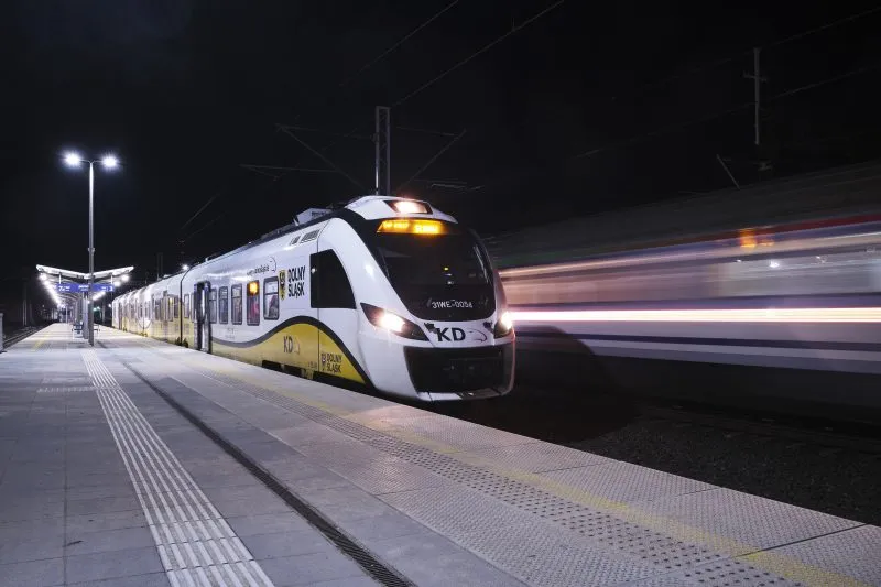 Pociąg kolej dolnośląskich mknący po torach przy peronie na tle nocnego nieba