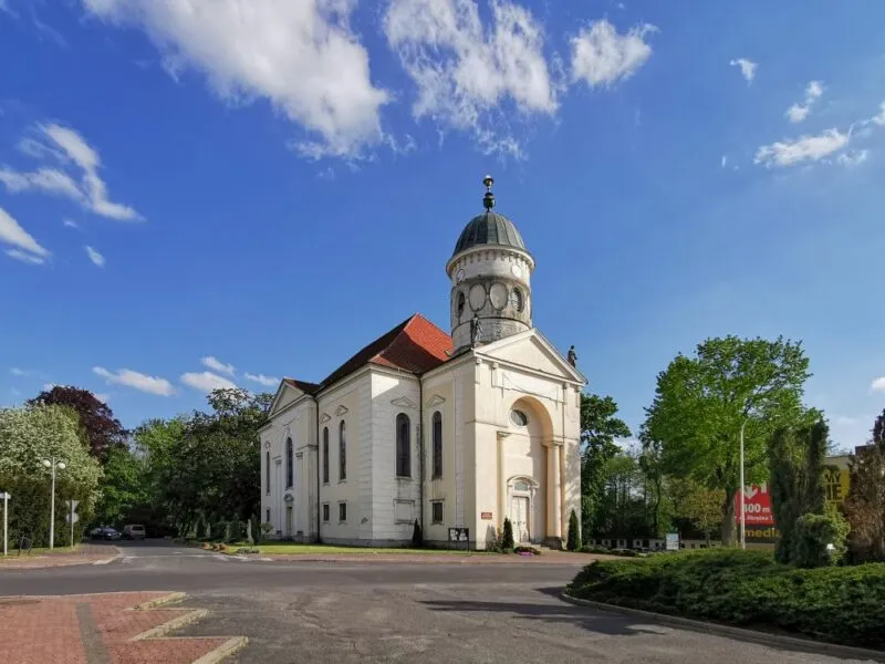 Biały kościół z wieżyczką w centrum na tle błękitnego nieba