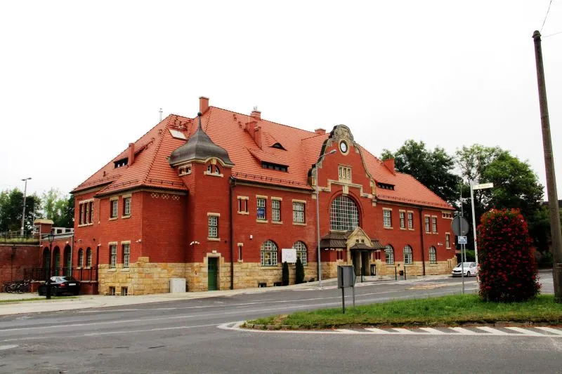 Budynek z czerwonej cegły, z czerwonym dachem i podmurówką z piaskowca