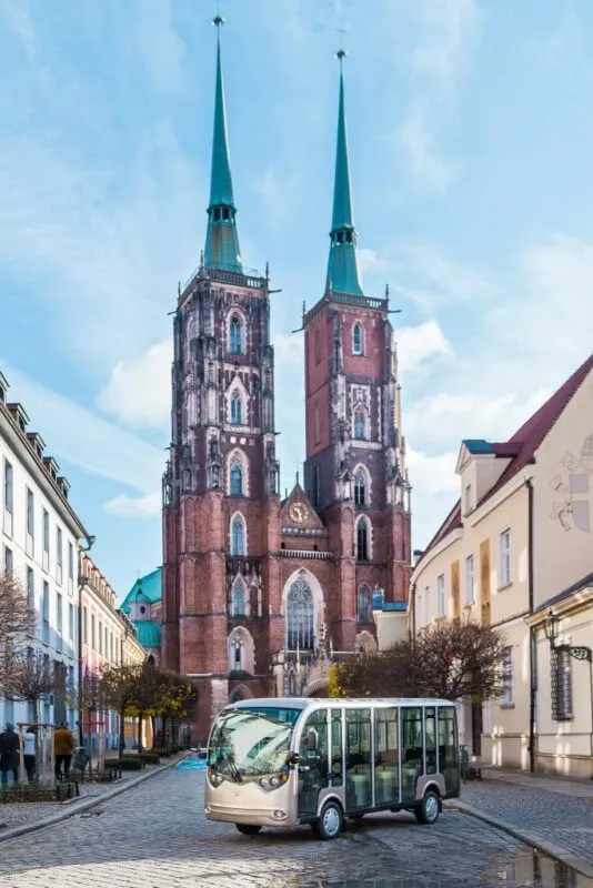 Katedra na Ostrowie Tumskim we Wrocławiu z 2 wieżami oraz zaparkowany meleks na starej kostce otaczanej 