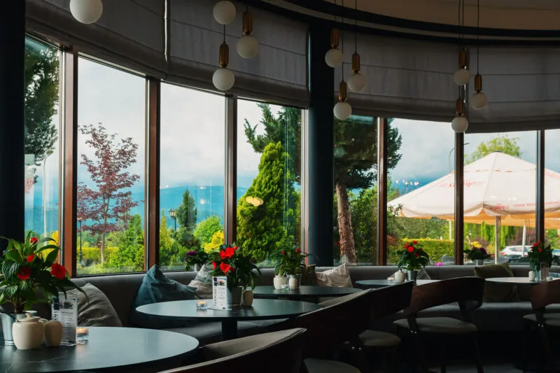 Przeszklona restauracja hotelu Kyriad Karkonosze ma ciemne stoliki, miękkie fotele i wiszące lampy, a za oknami rozciąga się zielony ogród z tarasem.