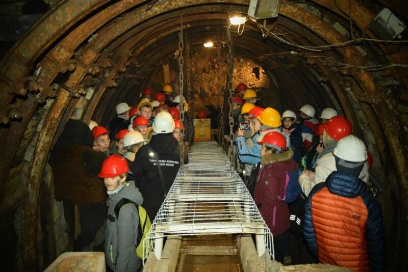 Turyści zwiedzający kopalnię stojący w jednym z oświetlonych tuneli.