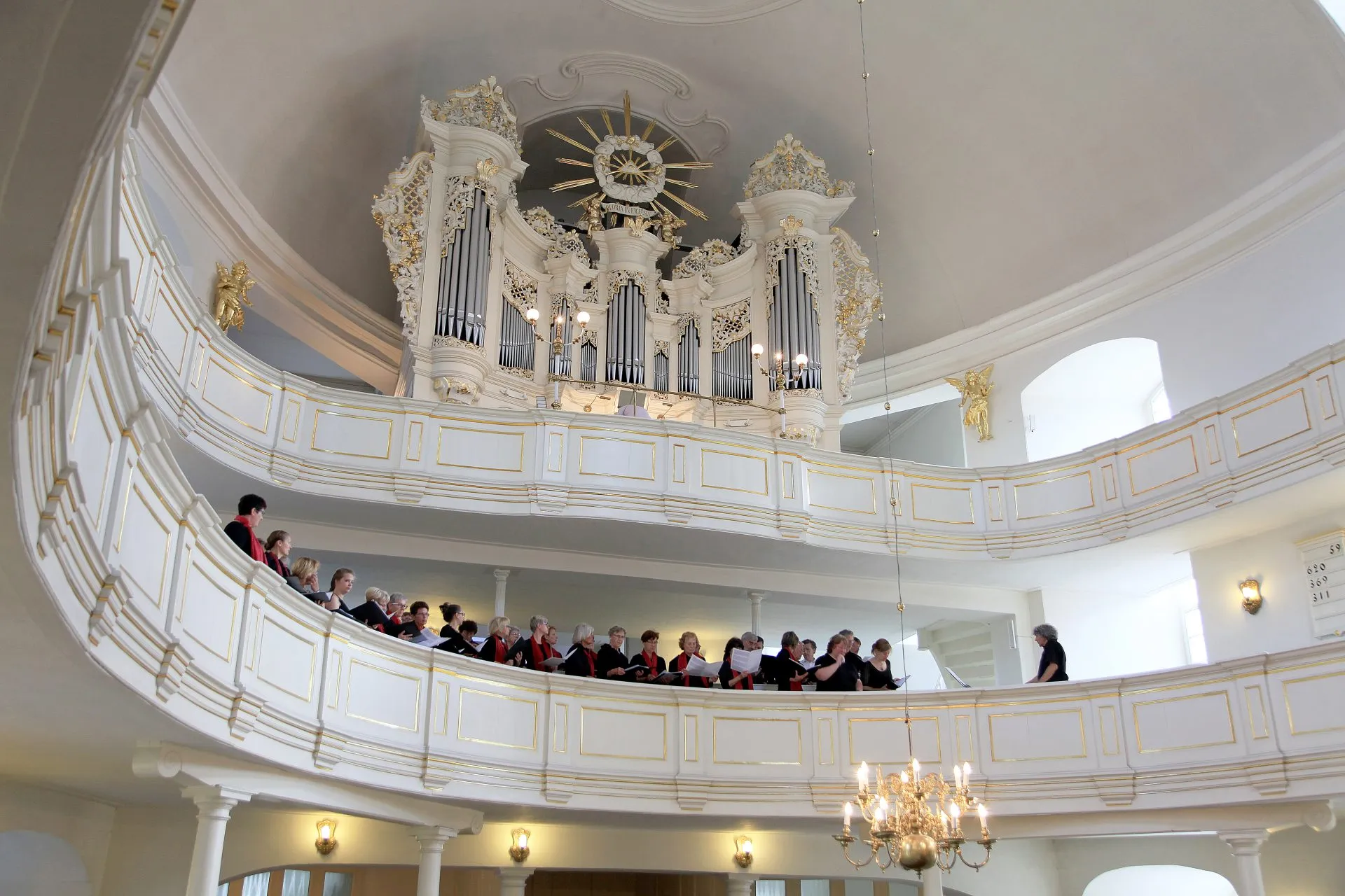 Prospekt organowy wraz z tylną lożą, na której stoi chór. Stylistyka utrzymana w kolorach biało-złotych.