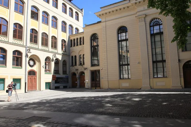 Główna elewacja synagogi z klasycystycznymi kolumnami oraz sąsiadujący budynek Uniwersytetu Wrocławskiego z kierunkiem judaistyki. Plac ten to serce wrocławskiej społeczności żydowskiej i miejsce wydarzeń kulturalnych.