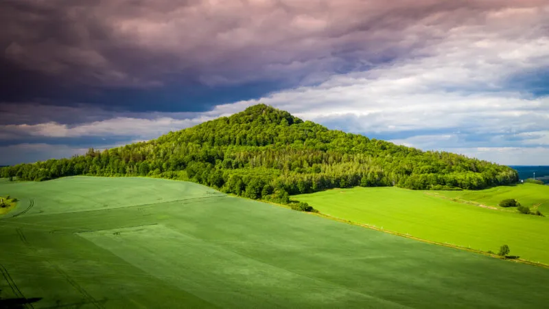 Widok z lotu ptaka na górę, polanę, w tle pochmurne niebo.