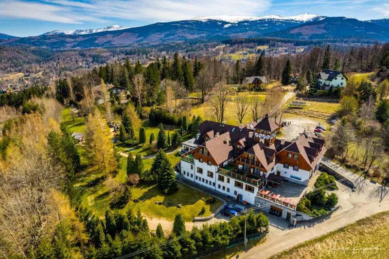 Duży budynek hotelowy w pięknym otoczeniu jesiennego krajobrazu, na tle gór, których szczyty pokryte są już śniegiem.