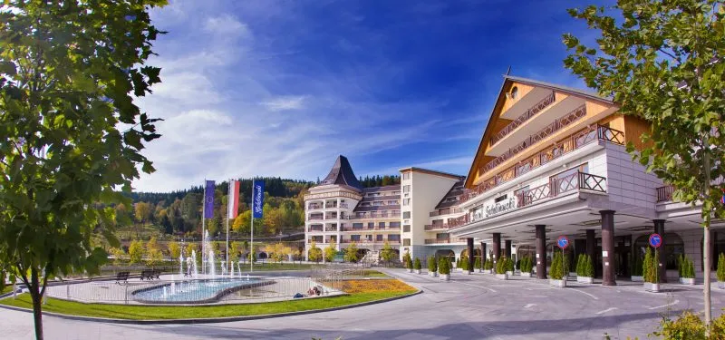 Główne wejście do hotelu. Przed budynkiem znajduje się fontanna oraz maszty z flagami. 