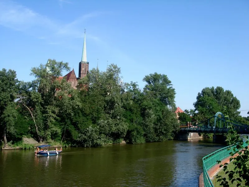 widok znad wody na katedrę ukrytą za drzewami, oraz na katamaran po lewej stronie zdjęcia