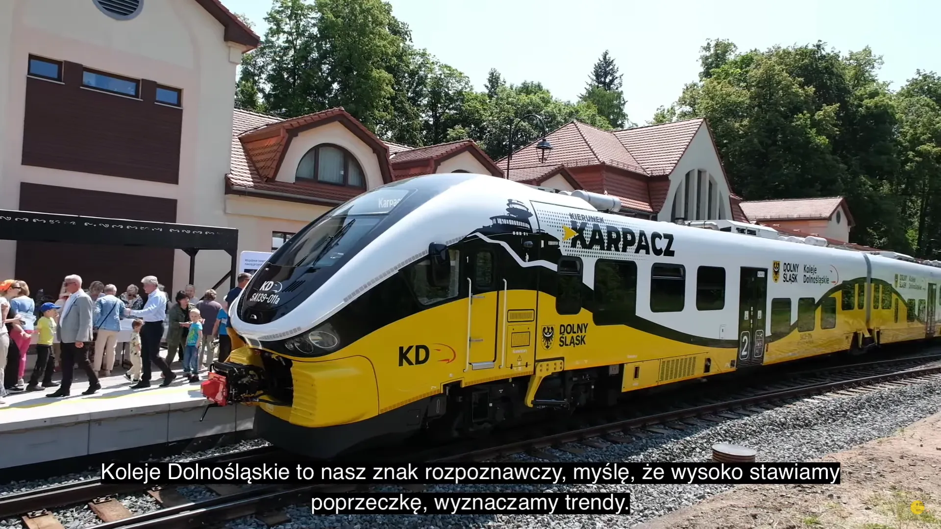 Zdjęcie przedstawia nowoczesny pociąg stojący przy peronie zabytkowej stacji kolejowej