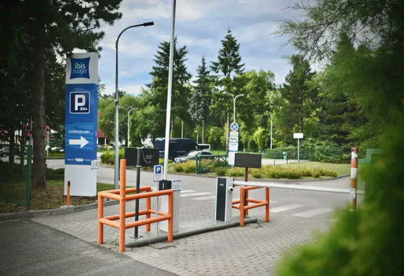 The entrance to the ibis Budget Wrocław Stadion hotel parking lot is marked with blue signs, an arrow, a barrier, and orange railings.