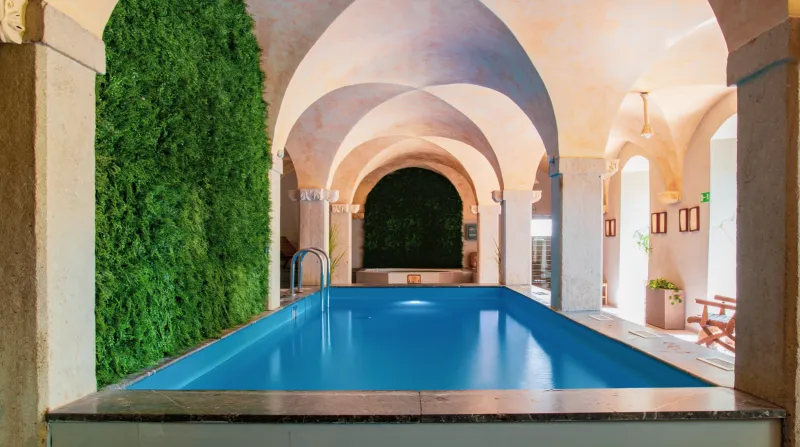 La piscina interior del Hotel Zamek na Skale en Trzebieszowice se encuentra bajo una bóveda de arcos, junto a paredes decoradas con vegetación vertical.