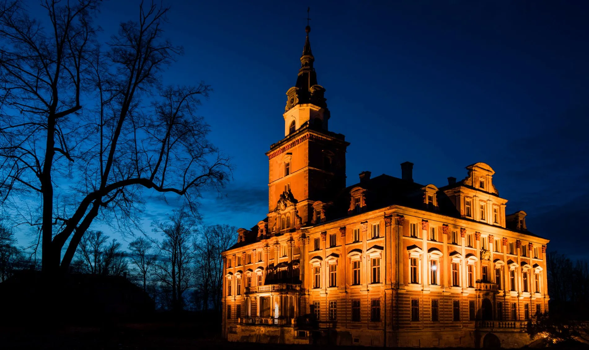 Widok na bryłę zabytkowego pałacu z podświetloną elewacją na tle wieczornego nieba