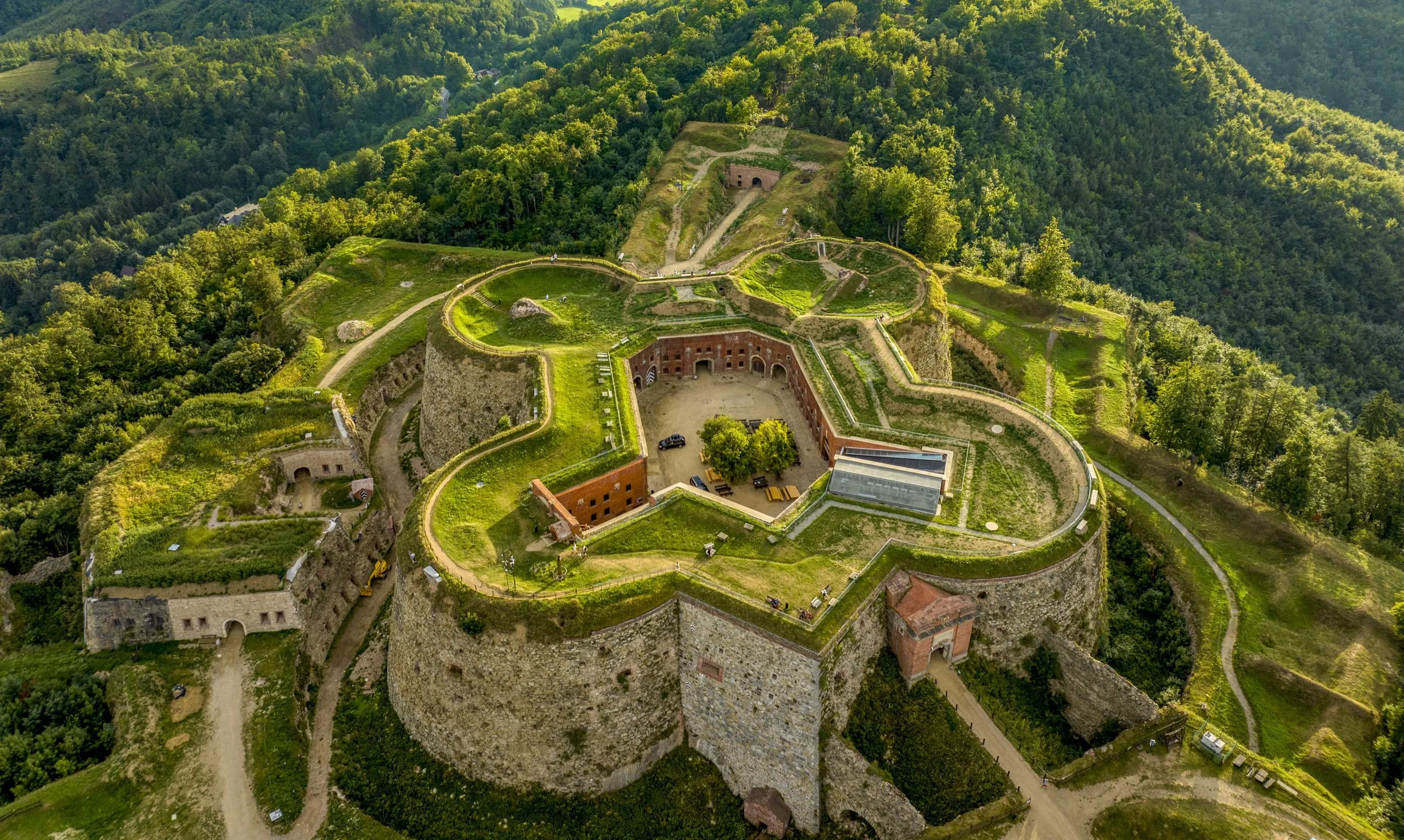 Majestatyczna twierdza górska na tle gór porośniętych gęstymi zielonymi lasami. 